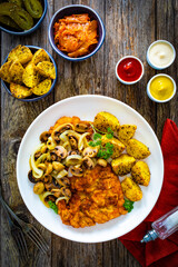Breaded fried pork chop with fried potatoes and mushrooms on wooden table
