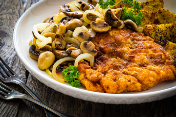 Breaded fried pork chop with fried potatoes and mushrooms on wooden table
