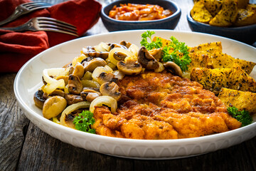Breaded fried pork chop with fried potatoes and mushrooms on wooden table
