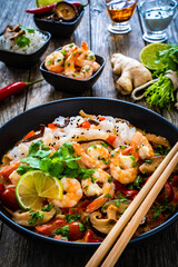 Tom Yum - Thai soup with prawns and rice noodles on black wooden table
