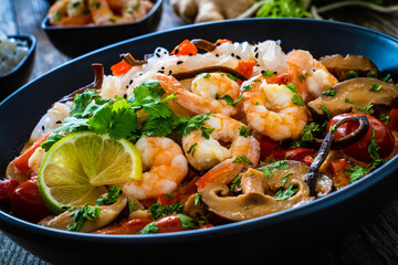 Tom Yum - Thai soup with prawns and rice noodles on black wooden table
