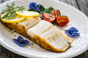 Fish dish - fried halibut with lemon and fresh vegetables on wooden table
