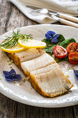 Fish dish - fried halibut with lemon and fresh vegetables on wooden table
