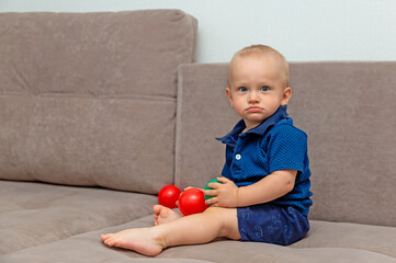 A little boy is sitting on the sofa with developing balls.  The child is safe at home