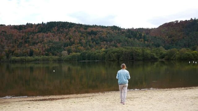 Woman walks by a lake and takes a photo of the mountain and the lake