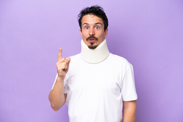 Young caucasian man wearing neck brace isolated on purple background intending to realizes the solution while lifting a finger up