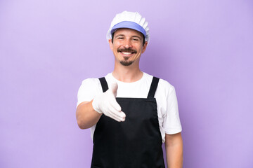 Fishmonger man wearing an apron isolated on purple background shaking hands for closing a good deal