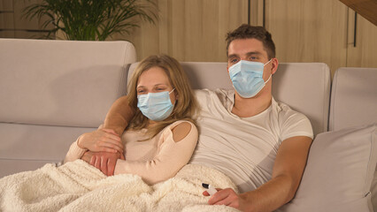 CLOSE UP: Couple wearing protective face masks and watching TV during sick leave