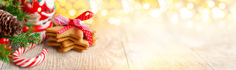Christmas gingerbread cookies with festive decoration, fir tree, pine cone and candy cane on wooden table. Christmas treats and decorations on festive bokeh background. Banner.