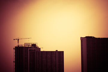 Abstract construction cranes and building silhouettes over sun at sunrise. vintage picture tone.