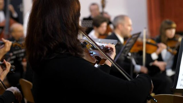 A woman violinist plays the violin against the background of the orchestra. Symphony concert at the Philharmonic. A violin in the hands of a violinist against the background of a music stand with note
