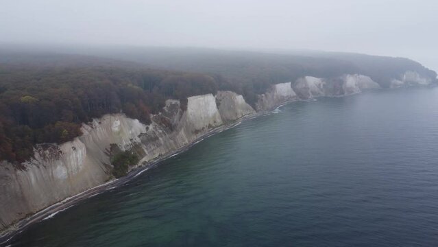pan drone shot of the Jasmund national park cliffs with its UNESCO world heritage beech forests in misty October weather