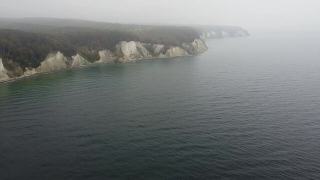 pan drone shot of the Jasmund national park cliffs with its UNESCO world heritage beech forests in misty October weather