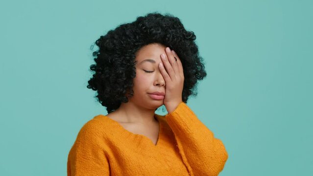 Upset worried curly hair woman slapping hand on face and expressing regret, blaming herself for troubles, feeling helpless studio. Facepalm, sorrow emotions on beautiful face of African American model
