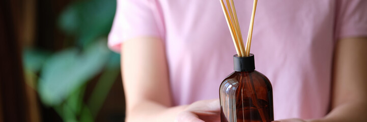 Woman holding jar with bamboo sticks of air freshener for home closeup