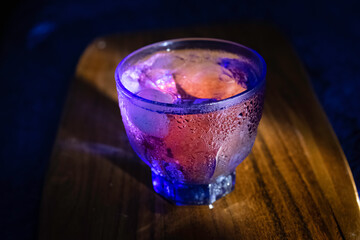 A transparent glass in the neon lights on the table background. Cocktail, party, and night life concept.