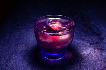 A transparent glass in the neon lights on the table background. Cocktail, party, and night life concept.