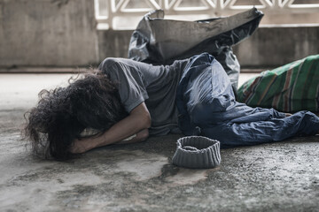 A homeless man sleeps on the street in the shadow of a building. and ask for help and money the troubles of the big modern city.