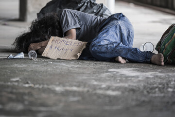 A homeless man sleeps on the street in the shadow of a building. and ask for help and money the troubles of the big modern city.
