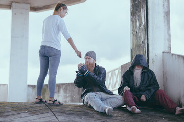  female giving money to poor or homeless people poverty beggar in the city sitting on the streets...