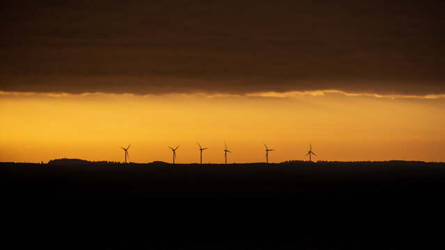 Atmospheric landscape sunrise image of wind turbines against deep orange sky