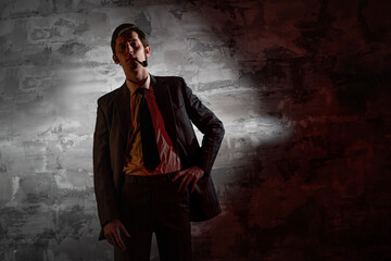 An arrogant man in a gray suit and tie smokes a pipe. Portrait in dark, noir and retro style
