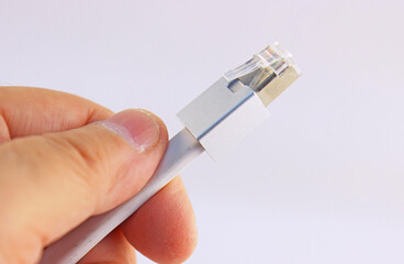 The hand holds a color-coded Ethernet wire with an RJ45 connector on a white background.Soft focus.