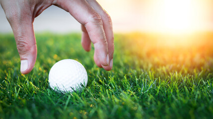 Golfer's hand holds golf ball close up on tee grass on blurred beautiful landscape of green...