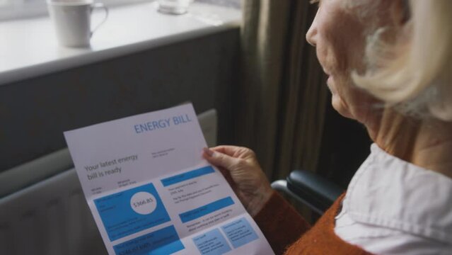 Close up of senior woman sitting in wheelchair by radiator at home looking at USA energy bill - shot in slow motion