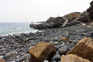 Kamienista plaża pod klifem z pofałdowaną ścianą.