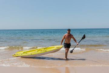 Male tourist with canoe walking near sea waves