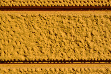 yellow stucco exterior elevation detail with rough steepled texture. deep grove pattern. surfaces, textures and patterns concept. facade macro detail. extreme closeup. buildings and architecture. 