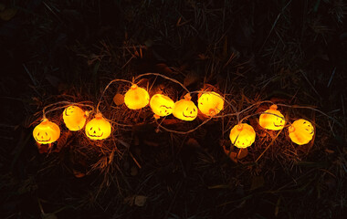 Glowing jack-o' lanterns garland on dark grass, abstract blurred natural background. symbol of Halloween holiday, Samhain sabbat. festive autumn season. top view - obrazy, fototapety, plakaty