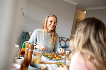 Two smiling blonde women eating a meal together at home