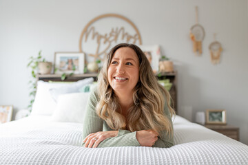 Smiling blonde woman lying on  the bed, looking away from camera