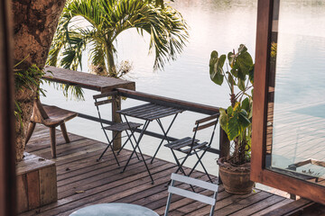 Empty wooden table and chairs on patio in tropical garden by the lake