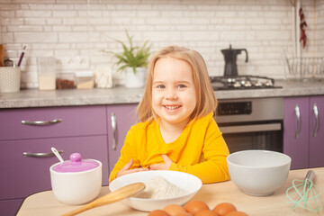 three-year-old girl in yellow jacket is preparing to cook food in kitchen. Portrait of happy child. smiles and looks into camera