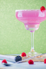 pink raspberry cocktail on a green background with raspberries and accessories for its preparation