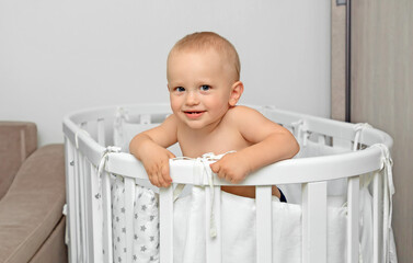Cute laughing baby standing in bed after a nap.  Charming little boy playing in his crib.  White furniture for the children's room