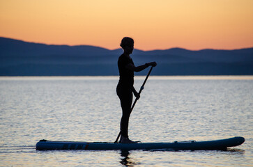 a young woman floats on a sapa on a mountain lake against the backdrop of sunset. Active recreation for a healthy lifestyle