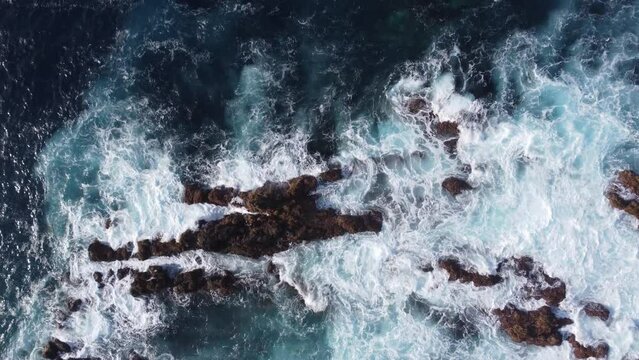 Drone shot of a wavy water crashing rocks