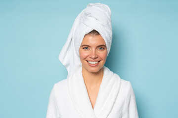 Close-up portrait of woman on blue background with head in bath towel dressed in bathrobe