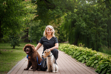 Portrait of glad woman with two dogs in park in summertime on vacations.
