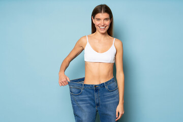 Slim woman pulling large oversize jeans to show results of her dieting and fitness workouts