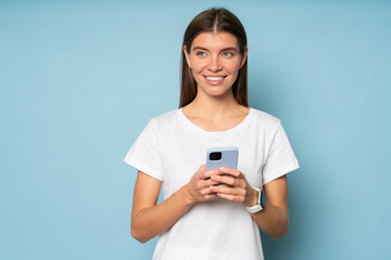 Woman using phone on blue background looking aside thinking over her respond in online chat