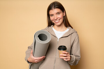 Casual woman having rest after fitness workout with rolled mat and coffee in hands