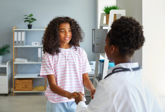 Children's medicine.Pediatrician. Excited teenage girl patient and doctor, who holds her hands as asign of support. Curly African American preteen girl having medical examination in doctor's office
