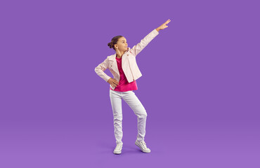 Cheerful funny stylish preteen girl having fun making dance moves isolated on purple background. Full length little girl in fashionable clothes posing on studio background. Children's fashion concept.