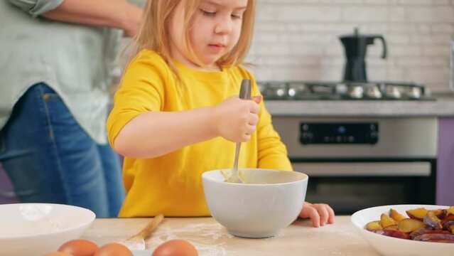 Mother and daughter cook pie in purple kitchen, training and development, interesting game and help. stir dough with spoon together