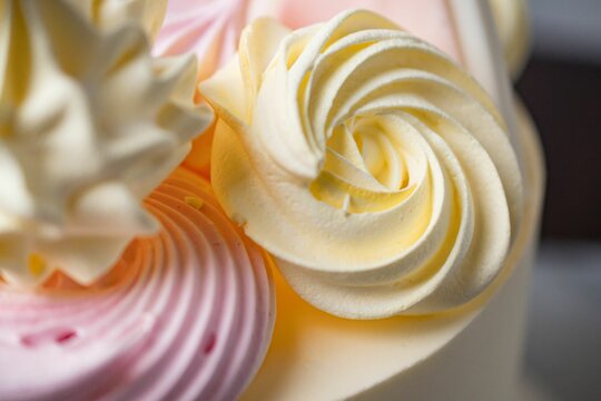 Naklejka Closeup shot of delicious pink and yellow swirl cream decorations on a cake